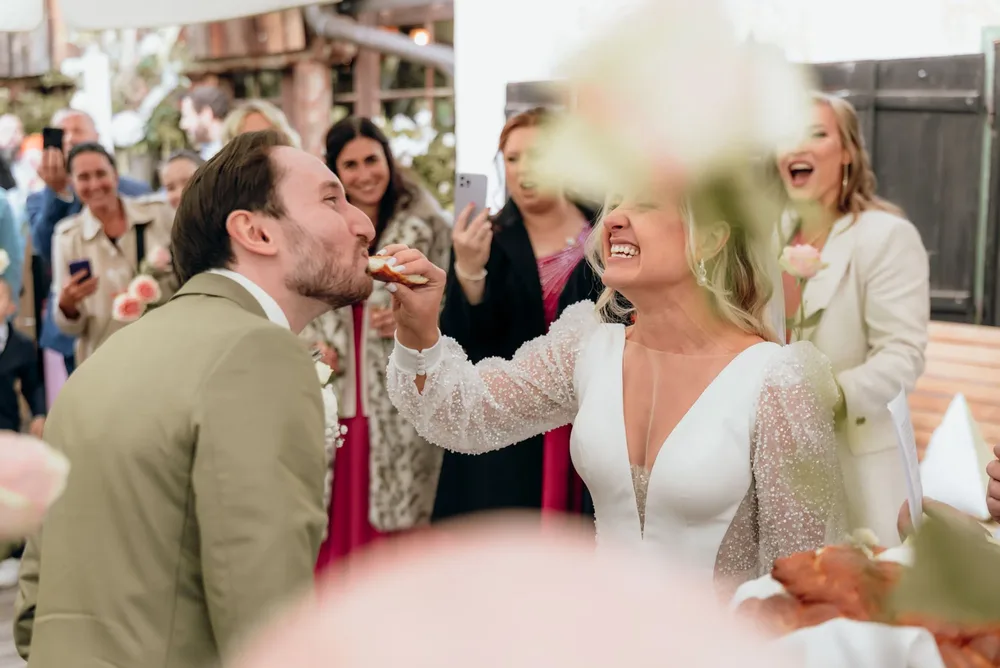 Braut füttert Bräutigam mit einem Stück Kuchen während der Hochzeit im Freihaus Brenner