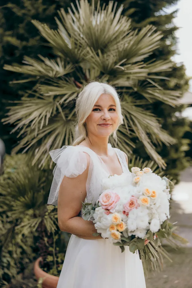 Braut in weißem Kleid mit blonden Haaren hält einen Brautstrauß in der Alten Gärtnerei München