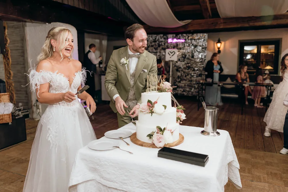 Braut und Bräutigam schneiden eine dreistöckige Hochzeitstorte im Freihaus Brenner am Tegernsee an