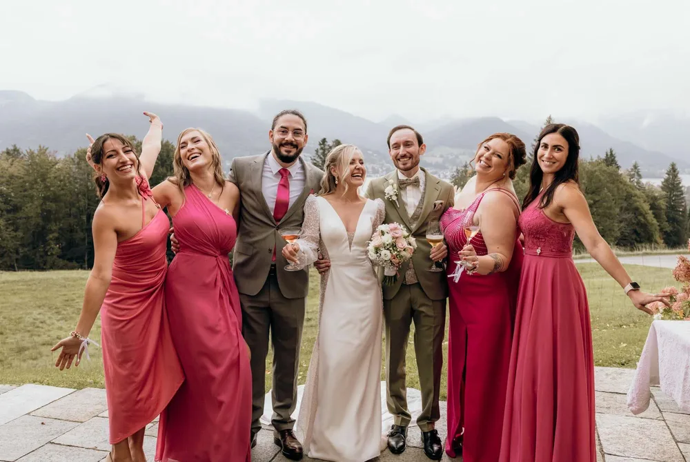 Brautpaar und vier Hochzeitsgäste in Pink lachend vor Bergkulisse am Tegernsee