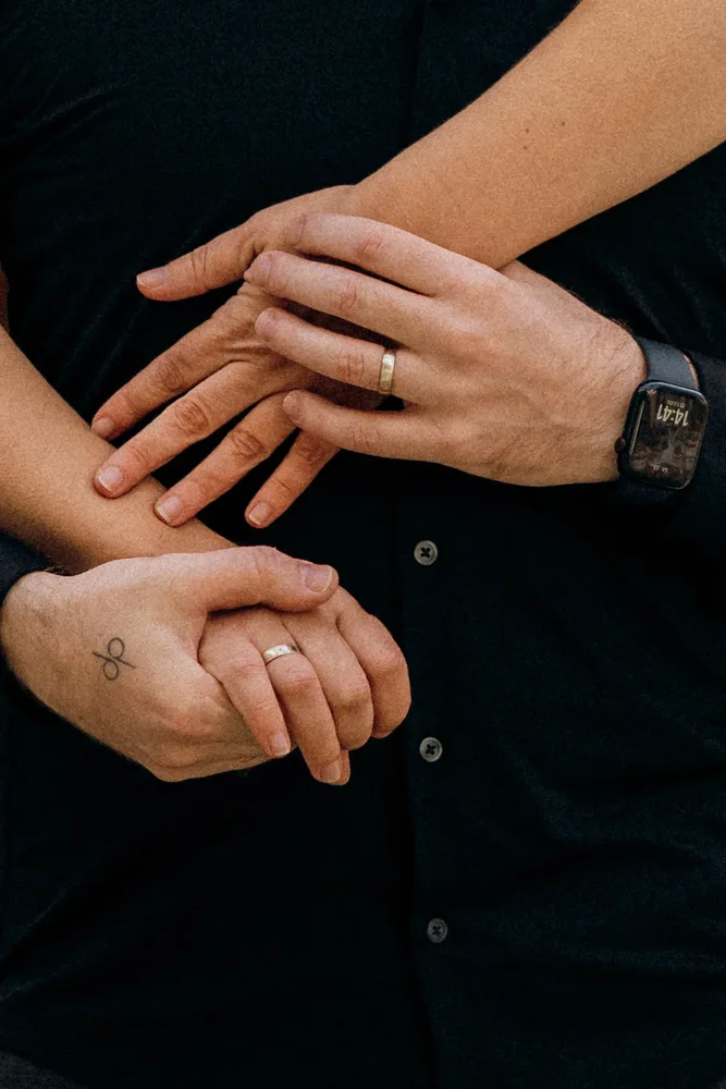 Claudia und Andy halten sich, beide Partner tragen Eheringe; ein Handgelenk hat eine Smartwatch. Das sind die Hochzeitsfotografen von MOKATI