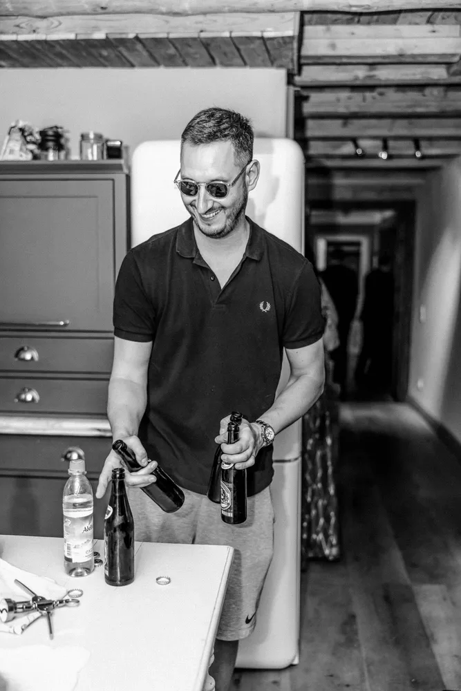 Lächelnder Mann in Sonnenbrille und Polohemd hält Bierflaschen beim Getting Ready vor der Hochzeit in der Alten Gärtnerei München