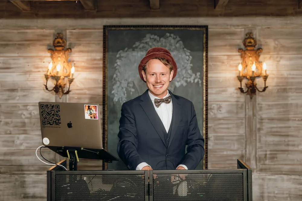 Jörn von SaxoBeatz lächelt hinter einem DJ-Pult bei einer Hochzeit im Freihaus Brenner
