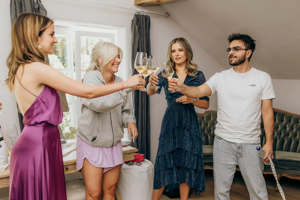 Vier Freunde stoßen beim Getting Ready mit Weißwein in einem rustikalen Raum an