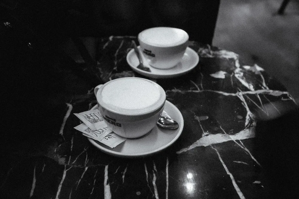 Zwei Tassen Cappuccino mit Milchschaum und Löffeln auf Untertassen stehen auf einem dunklen Marmortisch.